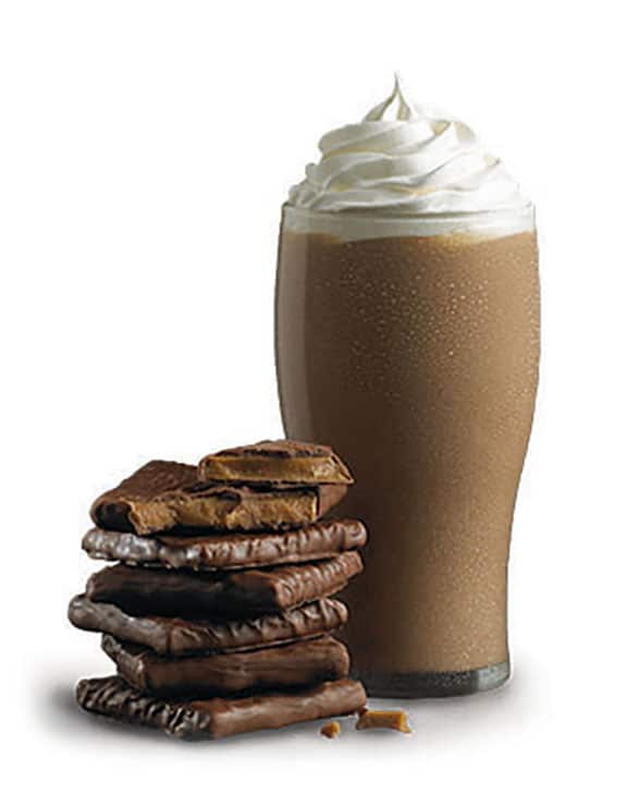 A cup of CAPPUCCINE Extreme Toffee Coffee with chocolate pieces and a whipped cream on top