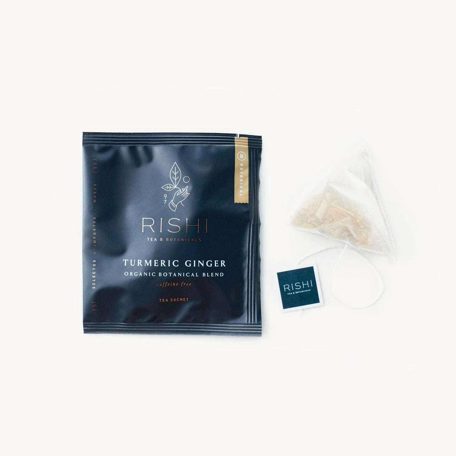 A packaged tea sachet with a label reading 'RISHI TURMERIC GINGER organic botanical blend', with an open sachet revealing a tea bag inside, placed on a white background.